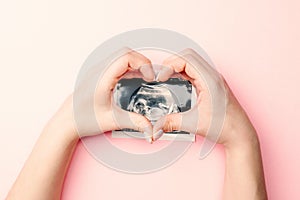 Ultrasound picture pregnant baby photo. Woman hands holding ultrasound pregnancy image on pink background. Concept of