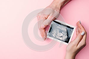 Ultrasound picture pregnant baby photo. Woman hands holding ultrasound pregnancy image on pink background. Concept of