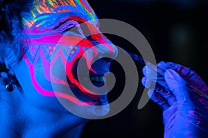 Ultraviolet black light glowing bodyart processing on young woman`s face. Pink and purple dyes in cold blue light