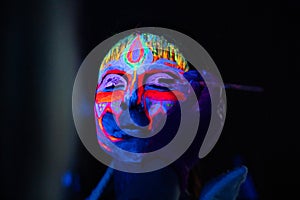 Ultraviolet black light glowing bodyart processing on young woman`s face. Pink and purple dyes in cold blue light