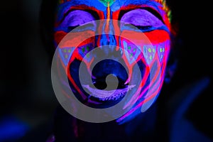 Ultraviolet black light glowing bodyart processing on young woman`s face. Pink and purple dyes in cold blue light