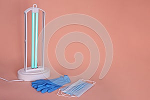 Ultraviolet lamp, medical masks and gloves on peach background, space for text