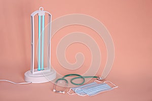 Ultraviolet lamp, medical masks and stethoscope on peach background, space for text