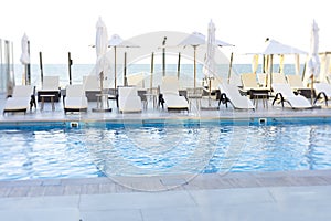 Umbrella and deck chair around outdoor swimming pool in hotel resort nearly sea beach ocean for travel vacation.