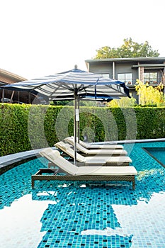 Umbrella and pool bed around outdoor swimming pool in hotel resort for travel holiday vacation