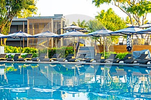 Umbrella and pool bed around outdoor swimming pool in hotel resort for travel holiday vacation