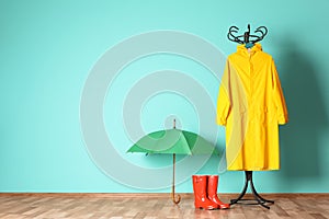 Umbrella, rain coat and boots near color wall