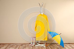 Umbrella, rain coat and rubber boots near beige wall. Space for text