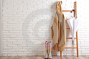 Umbrella, raincoat and rubber boots near white wall. Space for text