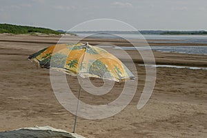 An umbrella from the sun on the sandy shore by the river