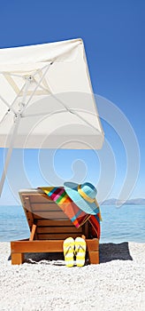 Umbrella and sunbed on the beach with blue hat, flip flop