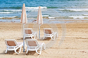 Umbrellas and chaise lounges on the beach. Empty plastic sunbeds near the sea. Tropical vacation, summer background.