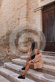 Una giovane ragazza bruna dai capelli fluenti in abito beige per le strade dei vicoli d& x27;Italia al tramonto con vasi photo
