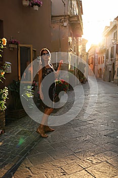 Una giovane ragazza bruna dai capelli fluenti in un tubino nero per le strade dei vicoli d& x27;Italia al tramonto con photo