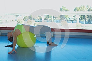 Una mujer morena realizando un estiramiento en la espalda en una pelota de pilates amarillo en un gimnasio photo