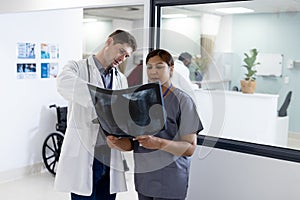 Unaltered portrait of diverse male and female doctor discussing x ray in hospital corridor