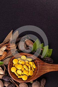 Unani medicine concept. Close-up view of herbal drugs in a wooden spoon and scattered herbs on black background in portrait mode