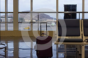 Unattended purple carry on suitcase by empty seat at airport terminal