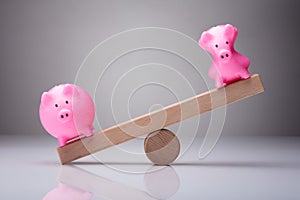 Unbalance Of Two Piggybanks On Wooden Seesaw