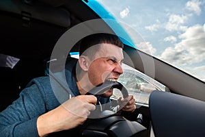An unbalanced, goosey man bites a car steering wheel from anger while driving in a traffic jam or after an accident. A nervous and