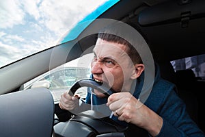 An unbalanced, goosey man bites a car steering wheel from anger while driving in a traffic jam or after an accident. A nervous and