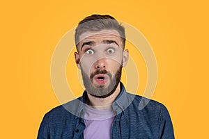 Unbelievable news. Portrait of bearded young guy opening mouth and eyes in shock, looking at camera on orange background