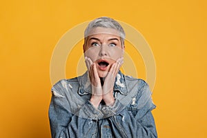 Unbelievable Offer. Shocked middle aged woman touching face in amazement, yellow background