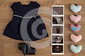 Unborn Baby Sonography and Girl Dress With Matching Shoes in a Flat Lay on Wooden Surface