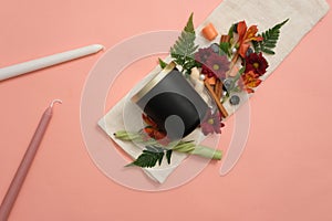 Unbranded black scented candles beside fresh flowers, colored candles, green leaves and cinnamon on a pink background with a white