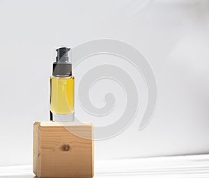 Unbranded bottle with body oil on wooden stand. Transparent glass container with dispenser. Repair, moisturizing for