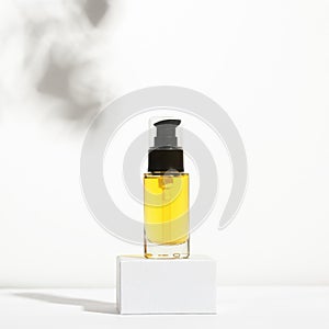 Unbranded glass container with dispenser on shadow background. Transparent bottle with oil for body on stand. Face serum