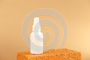 Unbranded white cosmetics spray bottle on golden podium on gold background. Front view, mockup. Cosmetic bottle container for