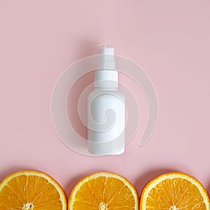 Unbranded white plastic spray bottle and orange slices border on pink background. Mockup. Skincare beauty and liquid antibacterial