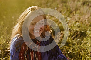 unbridled and cheerfully laughs a girl of natural beauty in an ethno cape sitting in a field on the grass