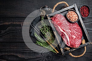 Unccoked rump steak or raw top sirloin beef meat steak. Black wooden background. Top view. Copy space
