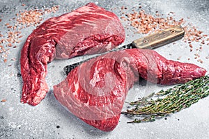 Unccoked tri-tip triangle roast, raw bottom sirloin steak on buther table with meat cleaver. Gray background. Top view