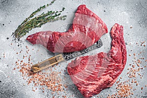 Unccoked tri-tip triangle roast, raw bottom sirloin steak on buther table with meat cleaver. Gray background. Top view