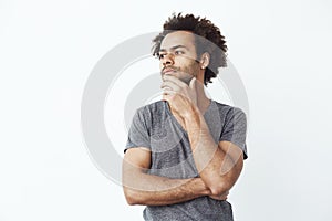 Uncertain african man thinking looking in side over white wall, deciding whether to buy some gadgets online or a student
