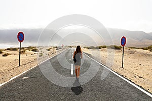 Uncertain future. Young alone woman advances with an uncertain step in empty asphalt desert road. Apocalypse concept