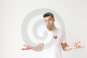 Uncertain hesitant bearded male in casual t shirt shruggs shoulders in bewilderment, tries to make decision about future