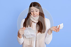 Uncertain pensive young woman holding pills, feeling indecisive about how to treated with them, reading instruction, squeeze