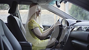 Uncertain young blond woman touching buttons in new luxurious car. Side view of attractive Caucasian lady examining