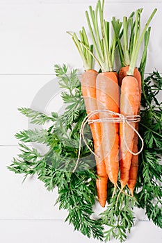 Unch of young carrots with green tops on white wooden vintage table, healthy food on mock up background top view