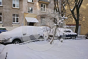 Uncleaned courtyards with heavy snowdrifts after snowfall in the city, cars under the snow