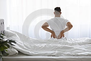 Uncomfortable Bed. Young Man Waking Up With Lower Back Pain, Rear View