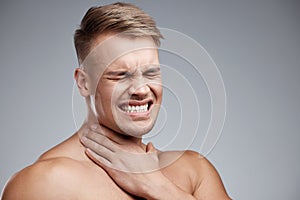 This is so uncomfortable. Studio shot of a muscular young man experiencing neck pain against a grey background.