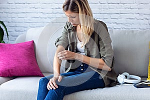 Uncomfortable young woman scratching her arm while sitting on the sofa at home