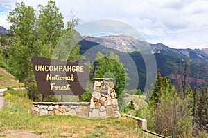 Uncompahgre National Forest border sign with United States Rocky Mountains in the background with lush forest mountainsides