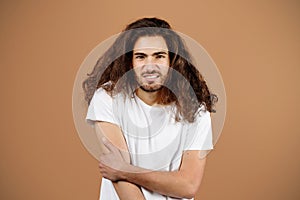 Unconfident hispanic guy with long hair posing over beige background photo