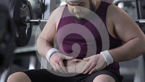 Unconfident overweight male in gym looking at his fat belly, weight loss dieting